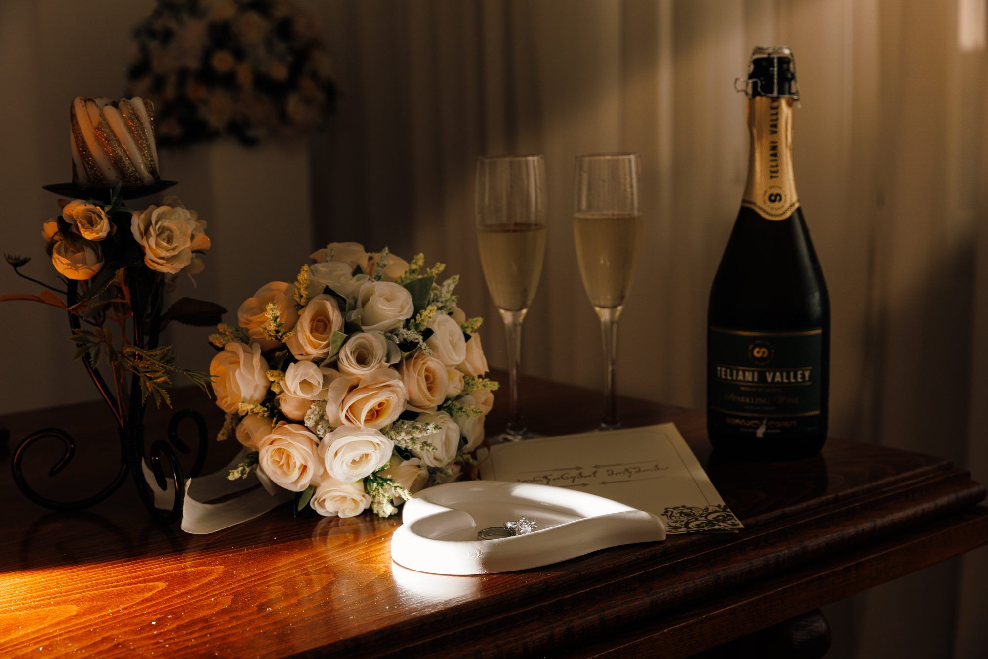 Bridal bouquet of cream roses, champagne glasses and a ring box on a wooden table